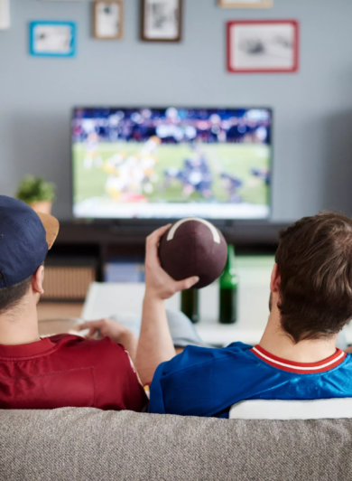 Three guys sitting on a couch watching football, holding a foam finger and a football